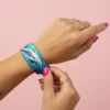 DELORA yunus desenli mavi elastik bilekliği bileğine takan kişinin elleri – QOOP Band deniz temalı unisex bileklik.