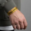 ASLAN BURCU İNCE ELASTİK BİLEKLİK Gri sweatshirt giyen erkeğin bileğinde altın sarısı 'Courage. Class. Lead.' yazılı Aslan burcu bileklik.