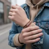 Kot ceket ve bej hoodie giyen erkeğin bileğinde kahverengi 'Power Patience Purpose' yazılı Oğlak burcu bileklik.
