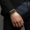 Siyah blazer ceket giyen erkeğin bileğinde Varex siyah ve altın geometrik bileklik.
