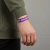 YAY BURCU İNCE ELASTİK BİLEKLİK Haki sweatshirt giyen erkeğin bileğinde mor 'Bold. Brave. Boundless.' yazılı Yay burcu bileklik.
